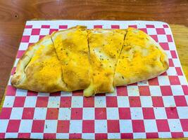 A delicious calzone topped with yellow cheese powder, cut into four pieces, served on a red and white checkered paper photo
