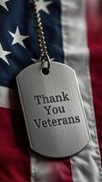 Metal dog tag with Thank You Veterans message displayed on American flag background signifies appreciation for military service photo