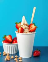 Delicious strawberry topped soft serve ice cream in a cup on a blue background with fresh strawberries and almonds photo