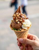 Delicious ice cream cone held by a person, featuring chocolate and vanilla flavors with toppings, enjoyed outdoors on a warm day photo