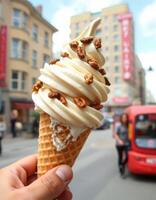 Hand holding a delicious ice cream cone topped with crunchy nuts on a busy city street in the daytime photo