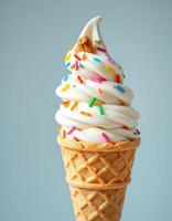 Soft serve ice cream cone topped with colorful sprinkles against a light blue background photo