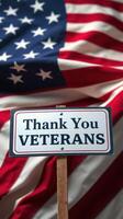 Sign expressing gratitude to veterans positioned in front of an American flag backdrop during a commemorative event photo