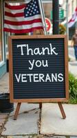 Sign expressing gratitude for veterans displayed on sidewalk with American flags in background photo