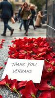 People walking in a busy urban area near red flower petals and a sign expressing gratitude to veterans photo
