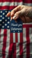 Hand holding tag expressing gratitude to veterans against a backdrop of an American flag, symbolizing respect and appreciation for service photo