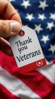 Thank you veterans tag held in hand against an American flag background during a patriotic event photo