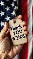 Hand holding a thank you tag for veterans against a backdrop of the American flag photo