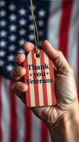 Hand holding thank you veterans tag in front of American flag background during a patriotic celebration photo