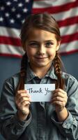 Young girl expresses gratitude in front of American flag with handwritten message in her hands photo