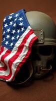 Military helmet adorned with an American flag draped over a skull on a wooden surface in dim lighting photo