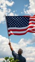 Proud individual waving an American flag against a backdrop of blue skies and fluffy clouds photo
