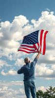 Man proudly raises American flag against a backdrop of clouds during a bright day in an outdoor setting photo