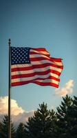American flag waves proudly against a clear blue sky with white clouds and evergreen trees in the background photo