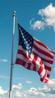 American flag waves under a clear blue sky with fluffy white clouds in the background photo