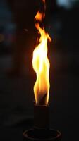 Fire burning brightly from a torch on a dark night under a subtle glow of distant lights photo