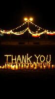 Illuminated message of gratitude displayed with candles and string lights at nighttime gathering photo