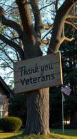 Sign honoring veterans displayed on a tree near a brick building during golden hour photo