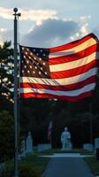 American flag waves proudly in evening light near memorial statues in a serene cemetery setting photo