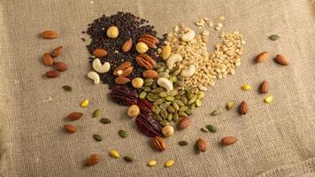 An overhead shot captures a diverse mix of nuts and seeds suspended in the air frozen in time amidst a backdrop of rustic burlap. The vivid yellows of flaxseeds dark browns. photo