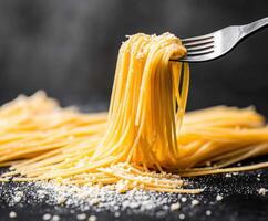 Delicious spaghetti served on a black surface with grated cheese and a fork lifting strands photo