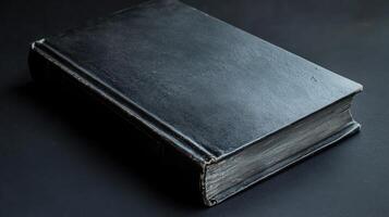 Classic black hardcover book on a dark surface with worn edges and a smooth texture photo