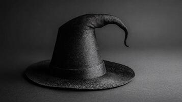 Elegant black witch hat resting on a dark surface, highlighting its pointed design and unique texture in the dim light photo
