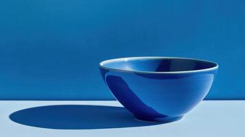 Bright blue bowl against a solid blue background casting a distinct shadow during daylight hours photo