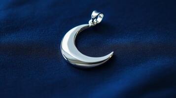 A silver crescent pendant on a blue cloth photo