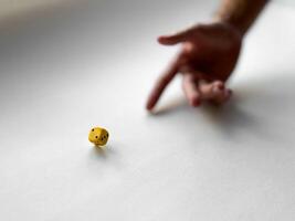 Hand rolling yellow dice on white surface representing chance and risk in game photo