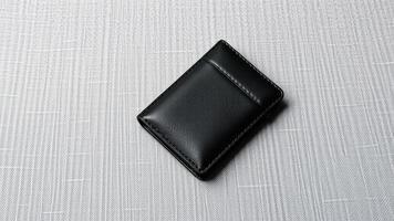 A black leather wallet with a zipper closure on a light gray fabric surface photo