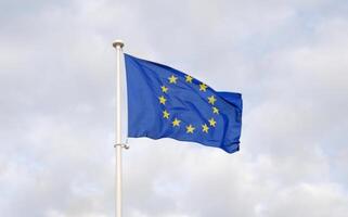 Flag of the European Union waving in the wind on flagpole against the blue sky. Close-up of single european flag with twelve yellow stars arranged in a circle. photo