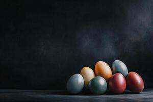 A still-life composition of jewel-toned Easter eggs, arranged elegantly on a dark, textured background. The warm highlights emphasize their glossy surface photo