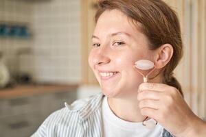 Young caucasian female using jade roller for skincare in home bathroom setting. photo