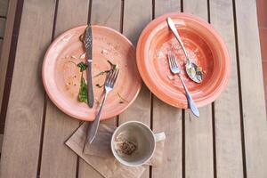 Empty orange plates and dirty coffee cup on wooden table after meal with used utensils. photo