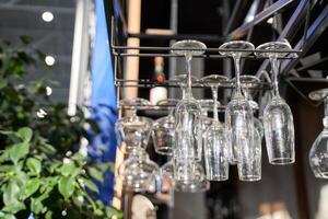 Empty wine glasses hanging upside down at a bar with sunlight and greenery in background. photo