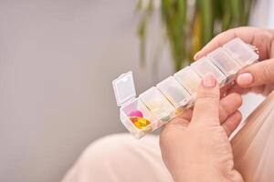 Female hand organizing weekly pillbox with colorful tablets and supplements in bright setting. photo