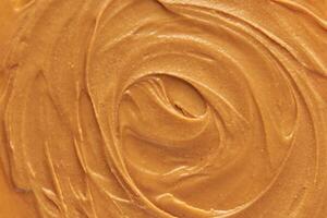 Smooth creamy peanut butter texture with swirls and rich nutty color close up view. photo