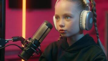 Streamer little Caucasian girl kid child daughter gamer in headphones talking to microphone digital gaming live stream influencer headset computer social media stream playing game home display video