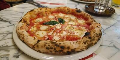 Neapolitan-style margherita pizza with charred crust, fresh mozzarella, tomato sauce, basil, and olive oil, served on a white plate for a classic Italian dining experience photo