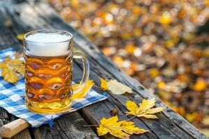 Glass of golden beer on a wooden table with autumn leaves and a blue checkered napkin outdoors photo