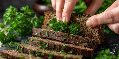 Hands holding slices of dark whole grain bread garnished with fresh parsley on a black background, highlighting a healthy and organic food concept photo