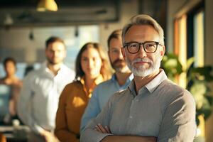 Five professionals are positioned in a bright office, showcasing a confident atmosphere. The leader in the forefront has gray hair and glasses, exuding experience. photo
