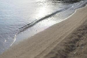 calm sea wave illuminated by the sun on a sandy beach on the seashore photo