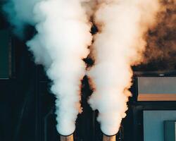 Aerial view of industrial smokestacks emitting white smoke into sky, surrounded by buildings. scene captures essence of industrial activity and environmental impact photo