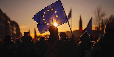 A silhouette of a person holding the European Union flag at sunrise during a protest, surrounded by a crowd in a cityscape photo