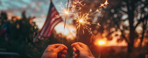 Hands holding sparklers with bright sparks against a sunset sky, with a blurred American flag in the background, symbolizing celebration and national pride photo