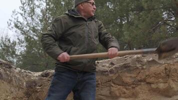 A man is digging in a forested area during winter, wearing a warm jacket and hat. He is using a shovel to break ground for a construction or landscaping project. video