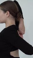 A dancer seated in a contemplative pose, hands reaching elegantly across the back. The black outfit and minimal setting accentuate the focus on flexibility and control. video