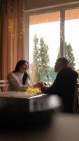 Romantic Connection by the Window A young couple shares an intimate moment, holding hands across a table adorned with fairy lights and flowers. Their silhouettes glow softly against the lush garden video